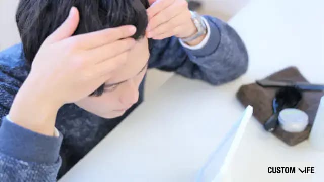 自身の髪の毛を触る男性