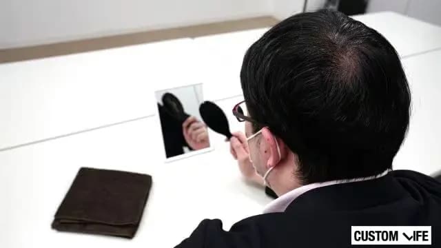 自分の頭皮を鏡でのぞき込む男性